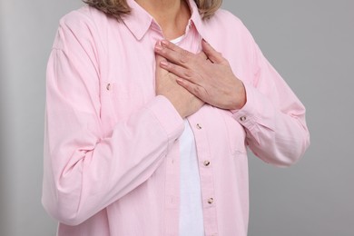 Photo of Heart attack. Senior woman suffering from pain in chest on light grey background, closeup