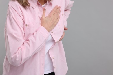 Heart attack. Senior woman suffering from pain in chest on light grey background, closeup. Space for text