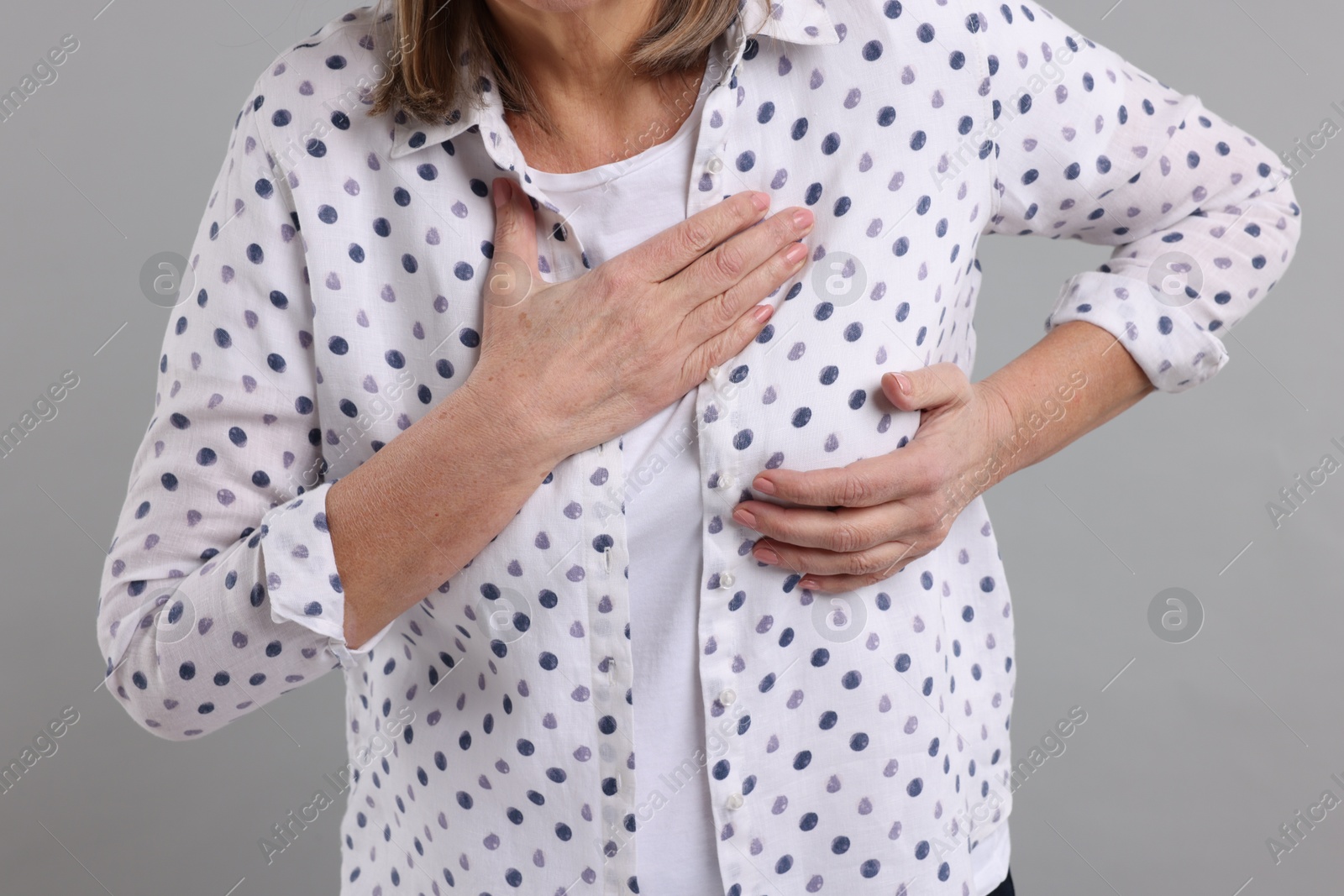 Photo of Heart attack. Senior woman suffering from pain in chest on light grey background, closeup