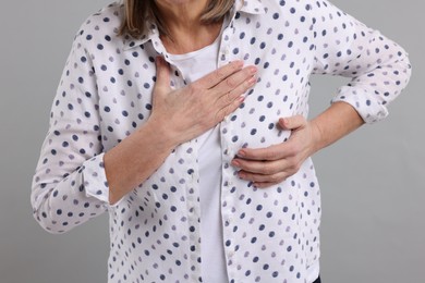 Heart attack. Senior woman suffering from pain in chest on light grey background, closeup