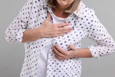 Photo of Heart attack. Senior woman suffering from pain in chest on light grey background, closeup