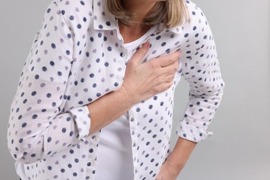 Heart attack. Senior woman suffering from pain in chest on light grey background, closeup