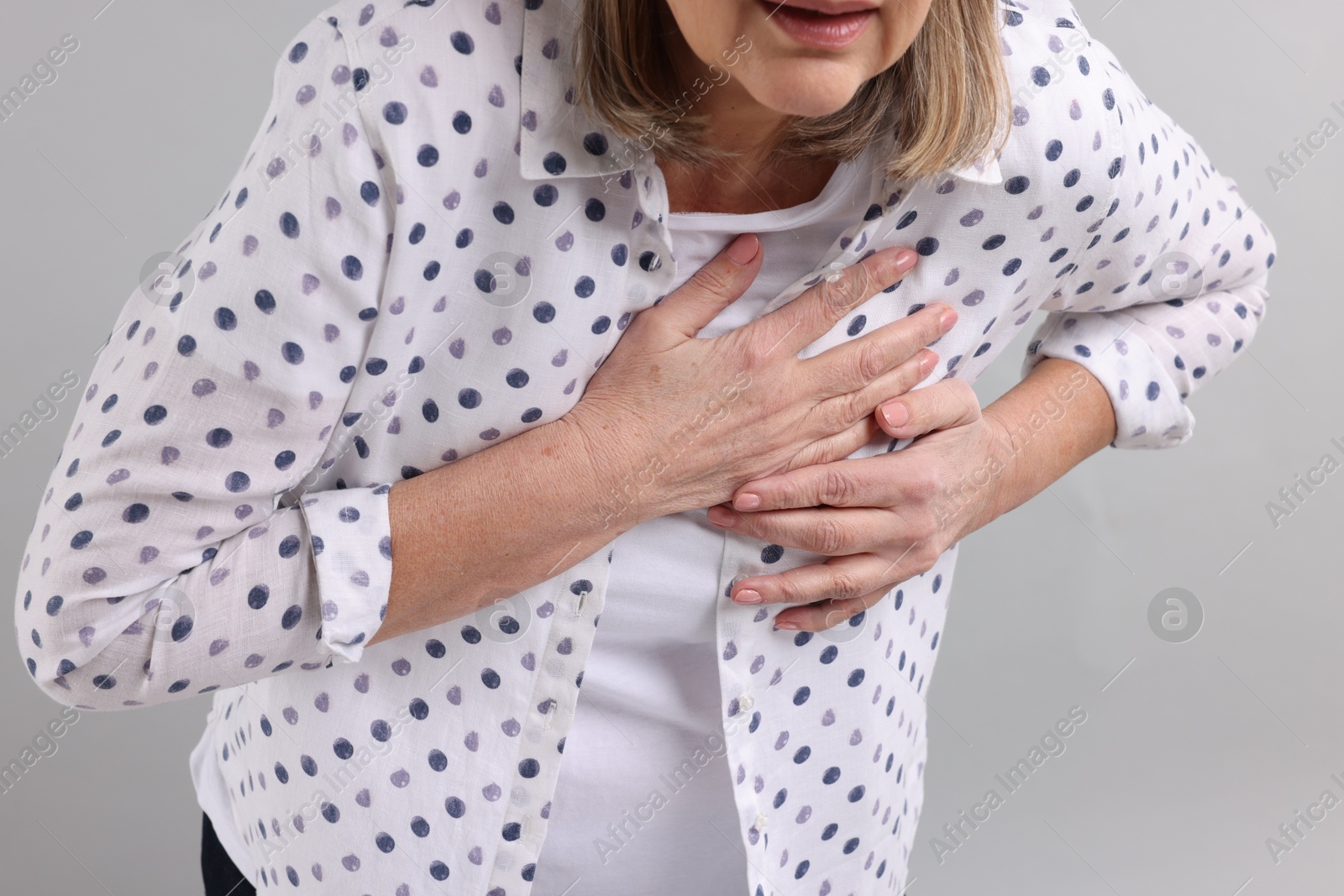 Photo of Heart attack. Senior woman suffering from pain in chest on light grey background, closeup