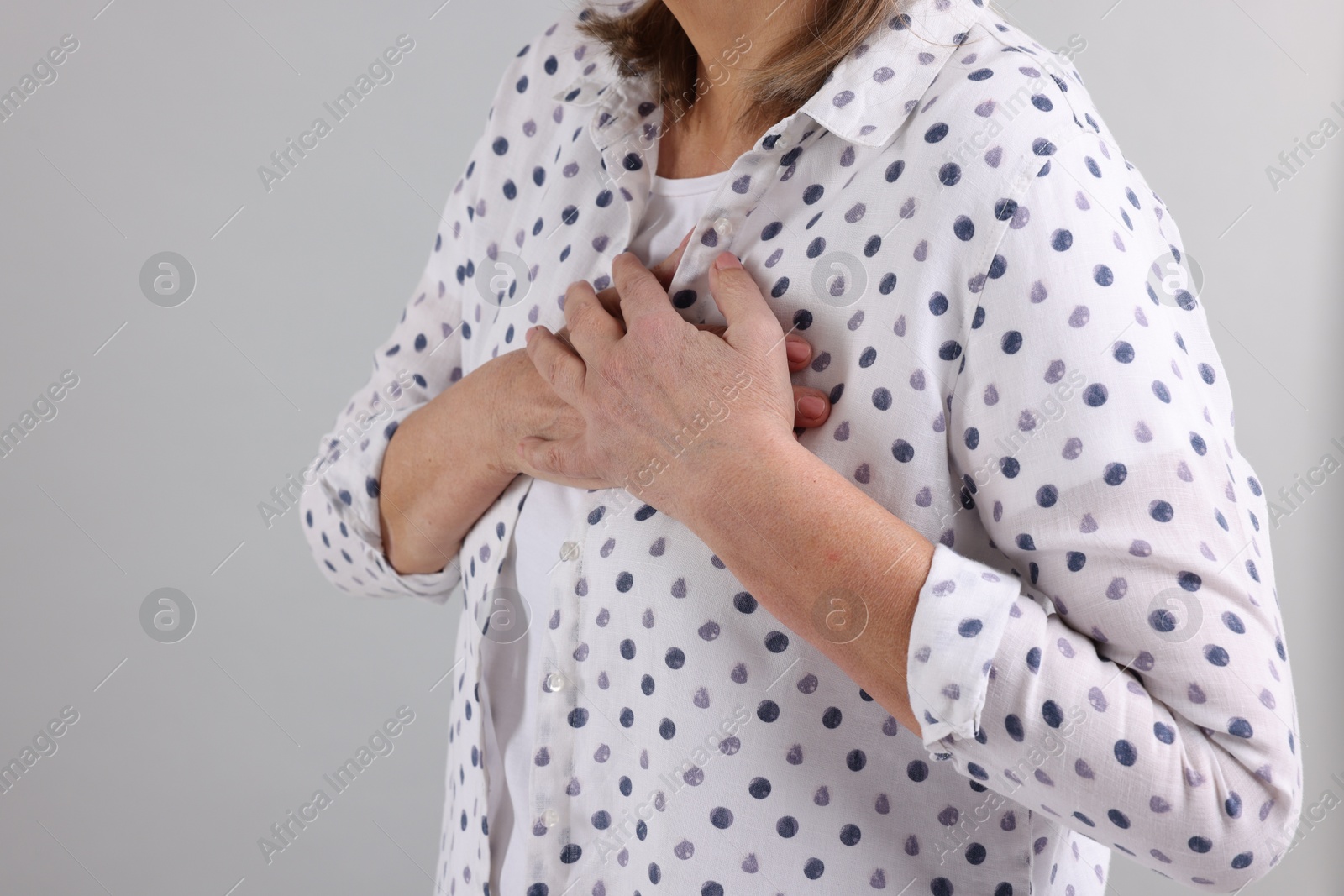 Photo of Heart attack. Senior woman suffering from pain in chest on light grey background, closeup