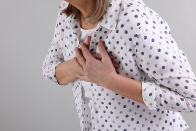 Photo of Heart attack. Senior woman suffering from pain in chest on light grey background, closeup