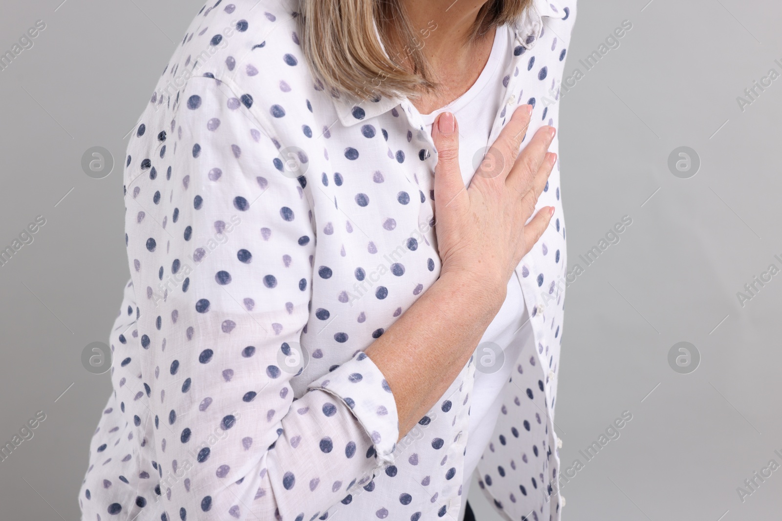 Photo of Heart attack. Senior woman suffering from pain in chest on light grey background, closeup