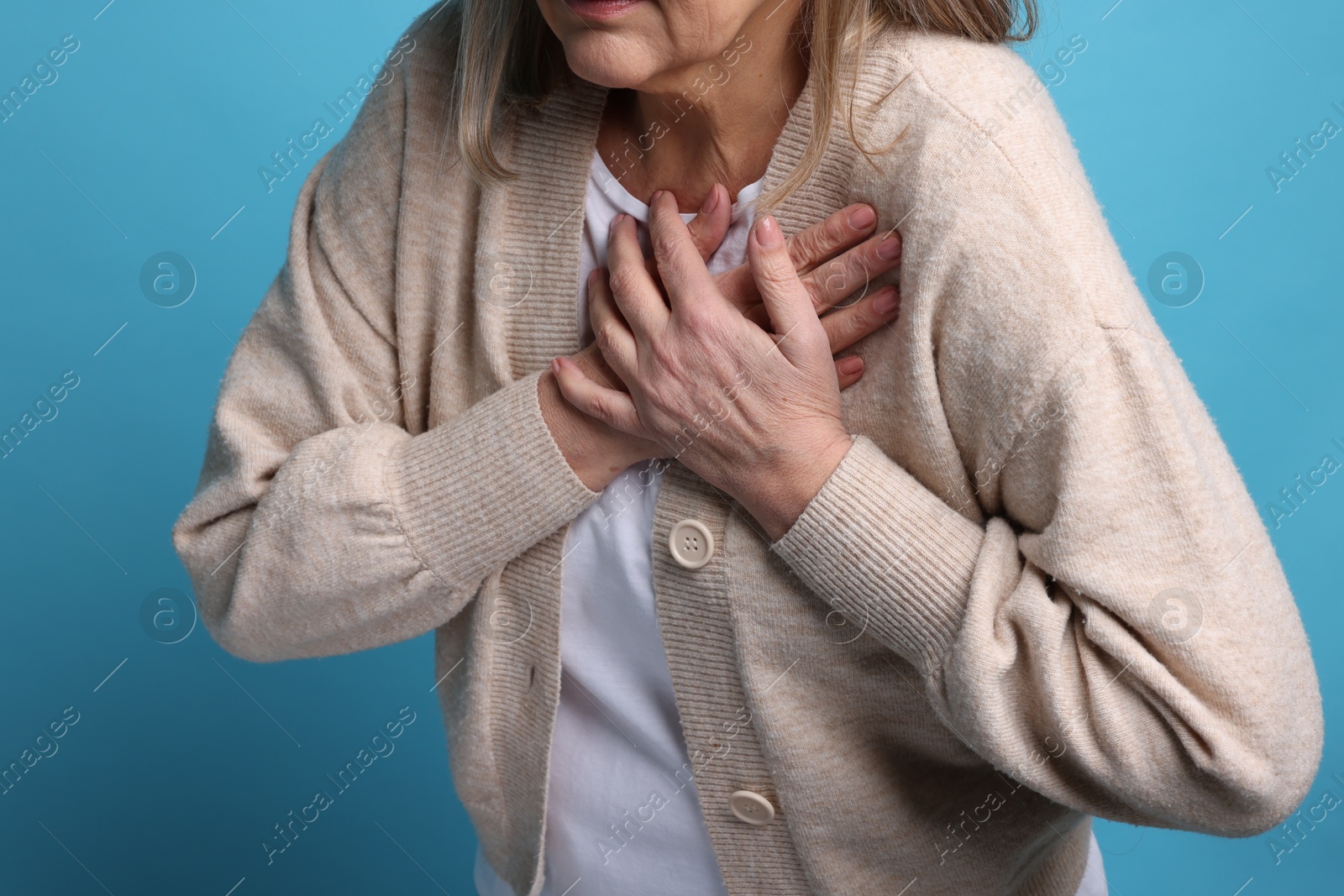 Photo of Heart attack. Senior woman suffering from pain in chest on light blue background, closeup