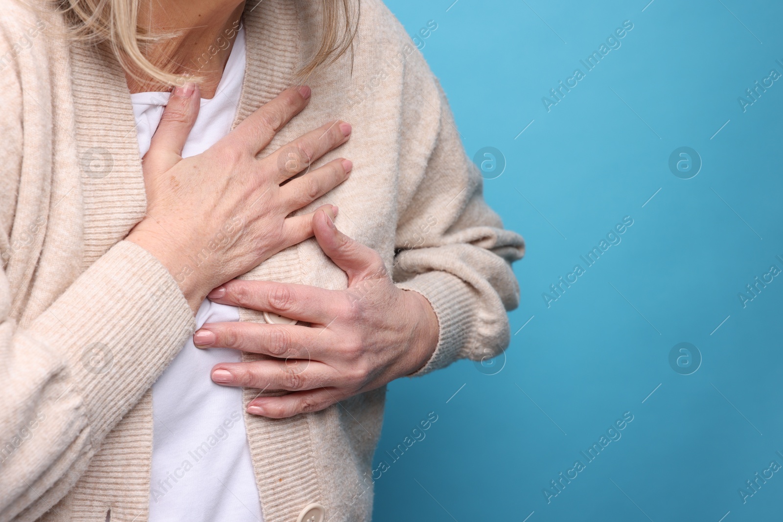 Photo of Heart attack. Senior woman suffering from pain in chest on light blue background, closeup. Space for text