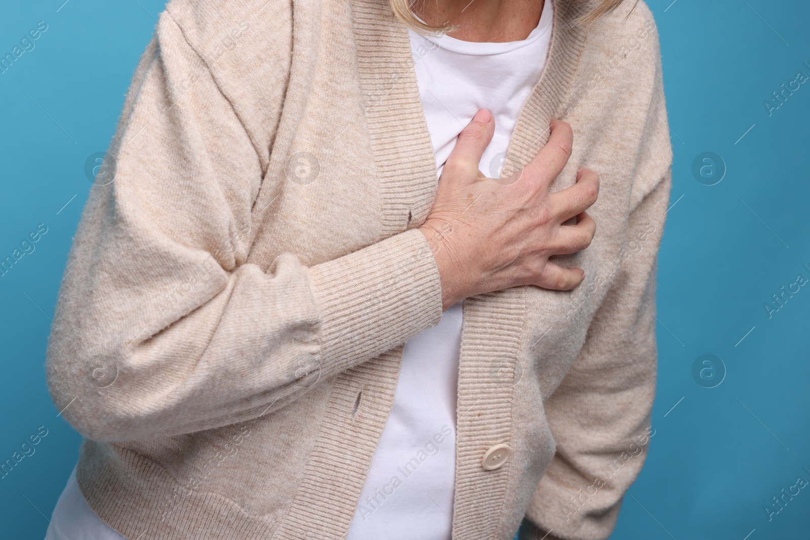 Photo of Heart attack. Senior woman suffering from pain in chest on light blue background, closeup