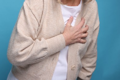 Heart attack. Senior woman suffering from pain in chest on light blue background, closeup