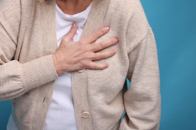 Heart attack. Senior woman suffering from pain in chest on light blue background, closeup