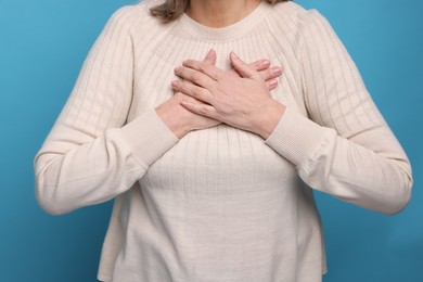 Heart attack. Senior woman suffering from pain in chest on light blue background, closeup