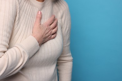 Heart attack. Senior woman suffering from pain in chest on light blue background, closeup. Space for text