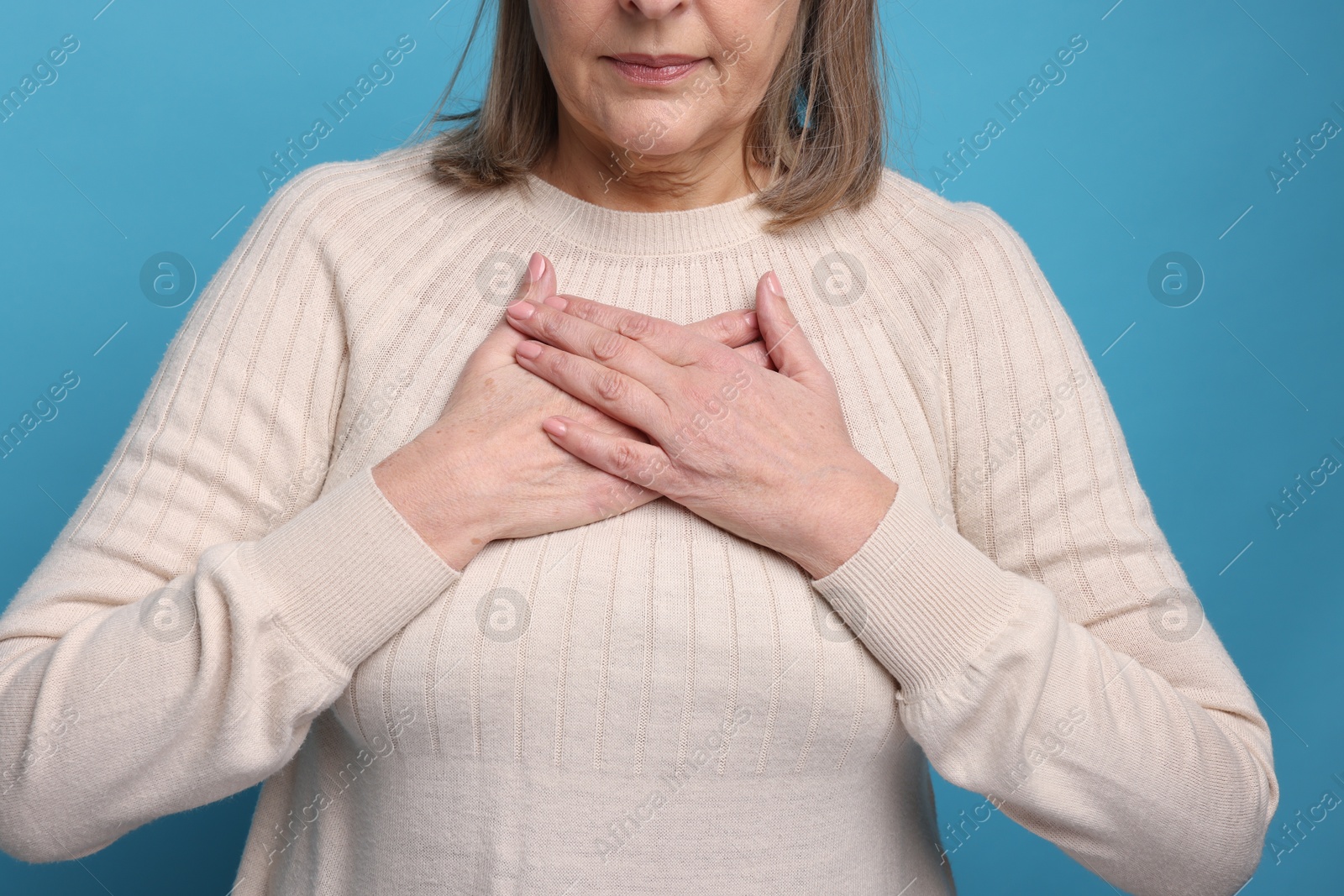 Photo of Heart attack. Senior woman suffering from pain in chest on light blue background, closeup