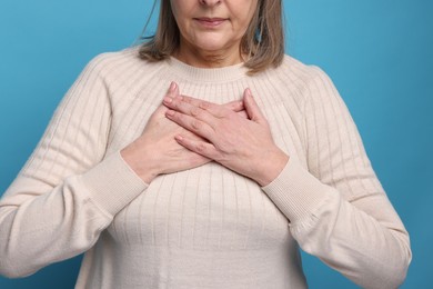 Heart attack. Senior woman suffering from pain in chest on light blue background, closeup