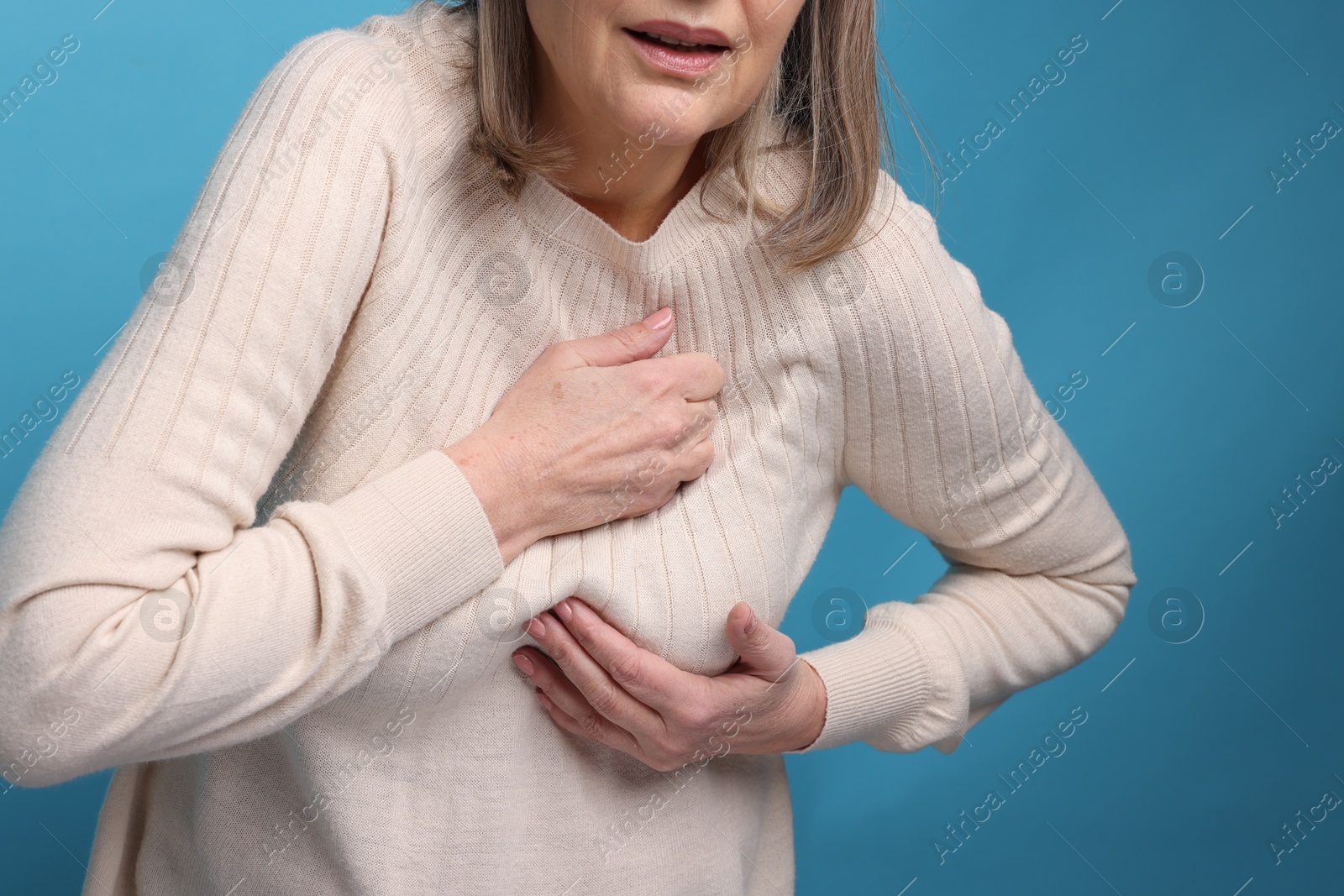 Photo of Heart attack. Senior woman suffering from pain in chest on light blue background, closeup