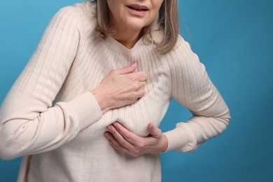 Heart attack. Senior woman suffering from pain in chest on light blue background, closeup