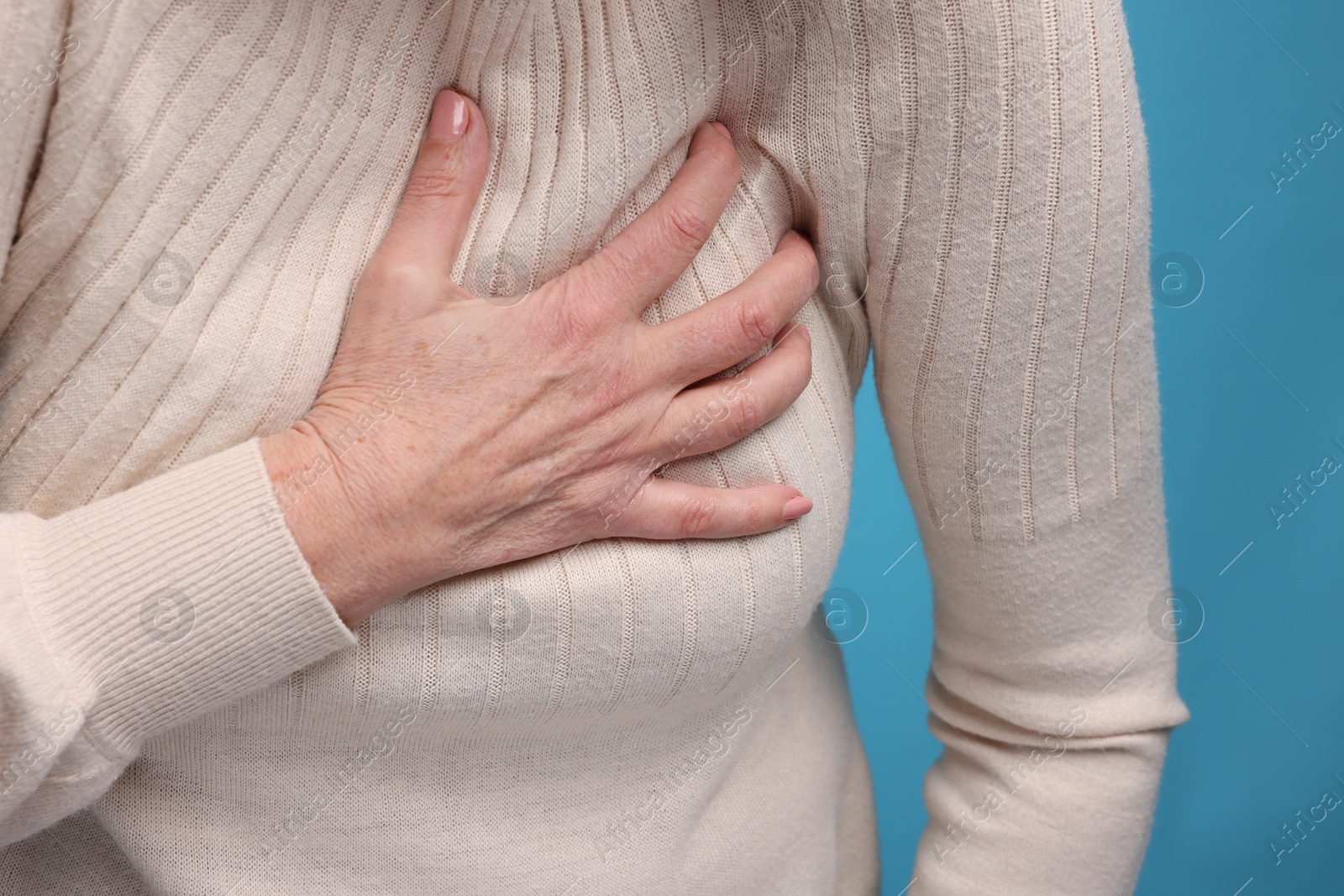 Photo of Heart attack. Senior woman suffering from pain in chest on light blue background, closeup