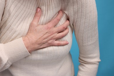 Heart attack. Senior woman suffering from pain in chest on light blue background, closeup