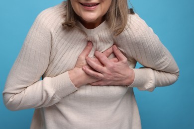 Heart attack. Senior woman suffering from pain in chest on light blue background, closeup