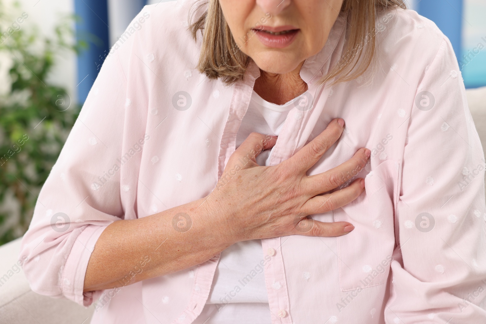 Photo of Heart attack. Senior woman suffering from pain in chest indoors, closeup