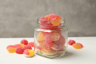 Photo of Tasty jelly candies in glass jar on white table against grey background, closeup