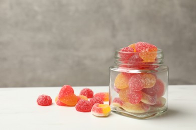 Photo of Tasty jelly candies in glass jar on white table against grey background. Space for text