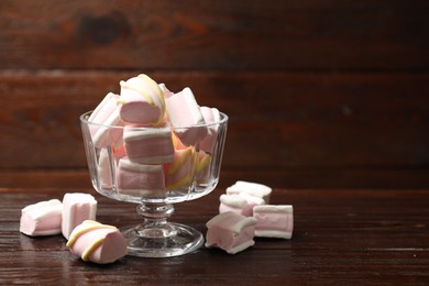 Photo of Tasty marshmallows in glass dessert bowl on wooden table, closeup. Space for text