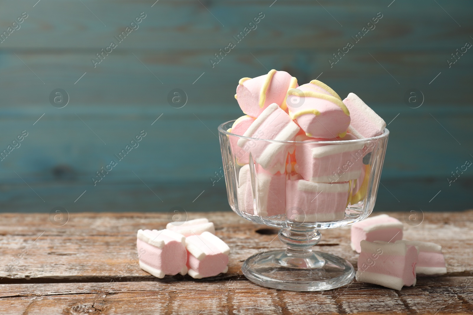 Photo of Tasty marshmallows in glass dessert bowl on wooden table, closeup. Space for text