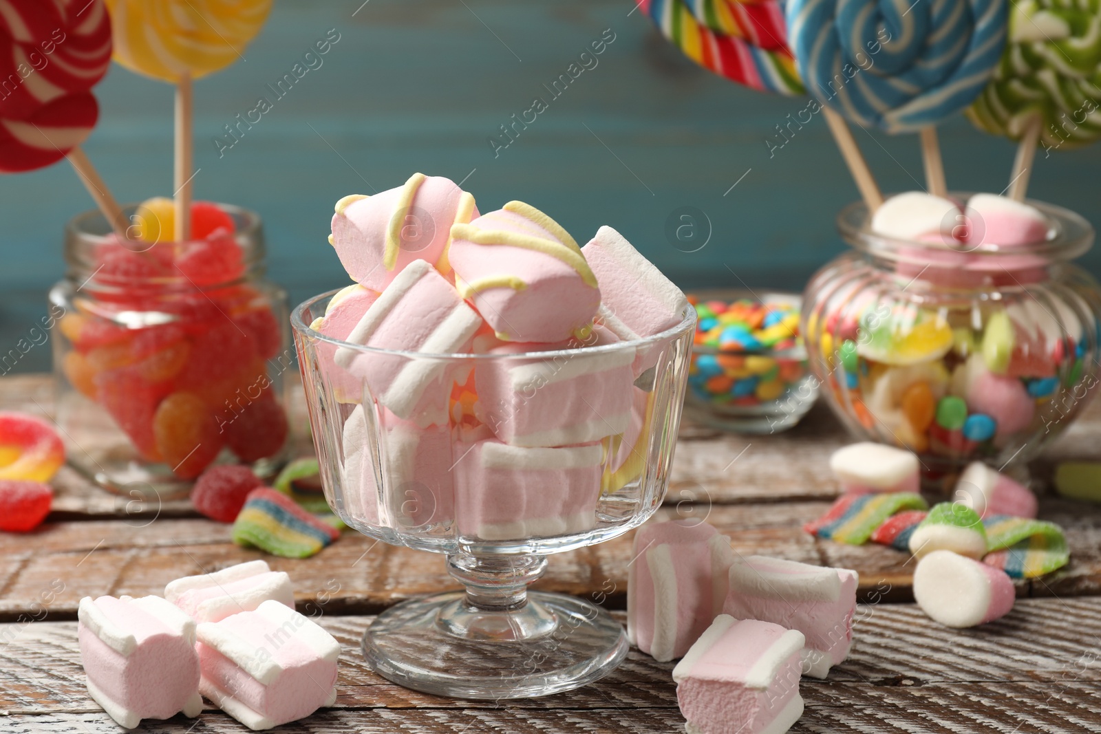 Photo of Tasty marshmallows in glass dessert bowl and candies on wooden table, closeup