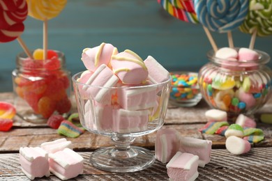 Photo of Tasty marshmallows in glass dessert bowl and candies on wooden table, closeup