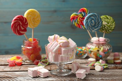 Photo of Tasty marshmallows in glass dessert bowl and candies on wooden table