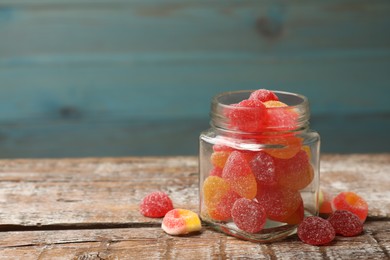 Photo of Tasty jelly candies in glass jar on wooden table, closeup. Space for text