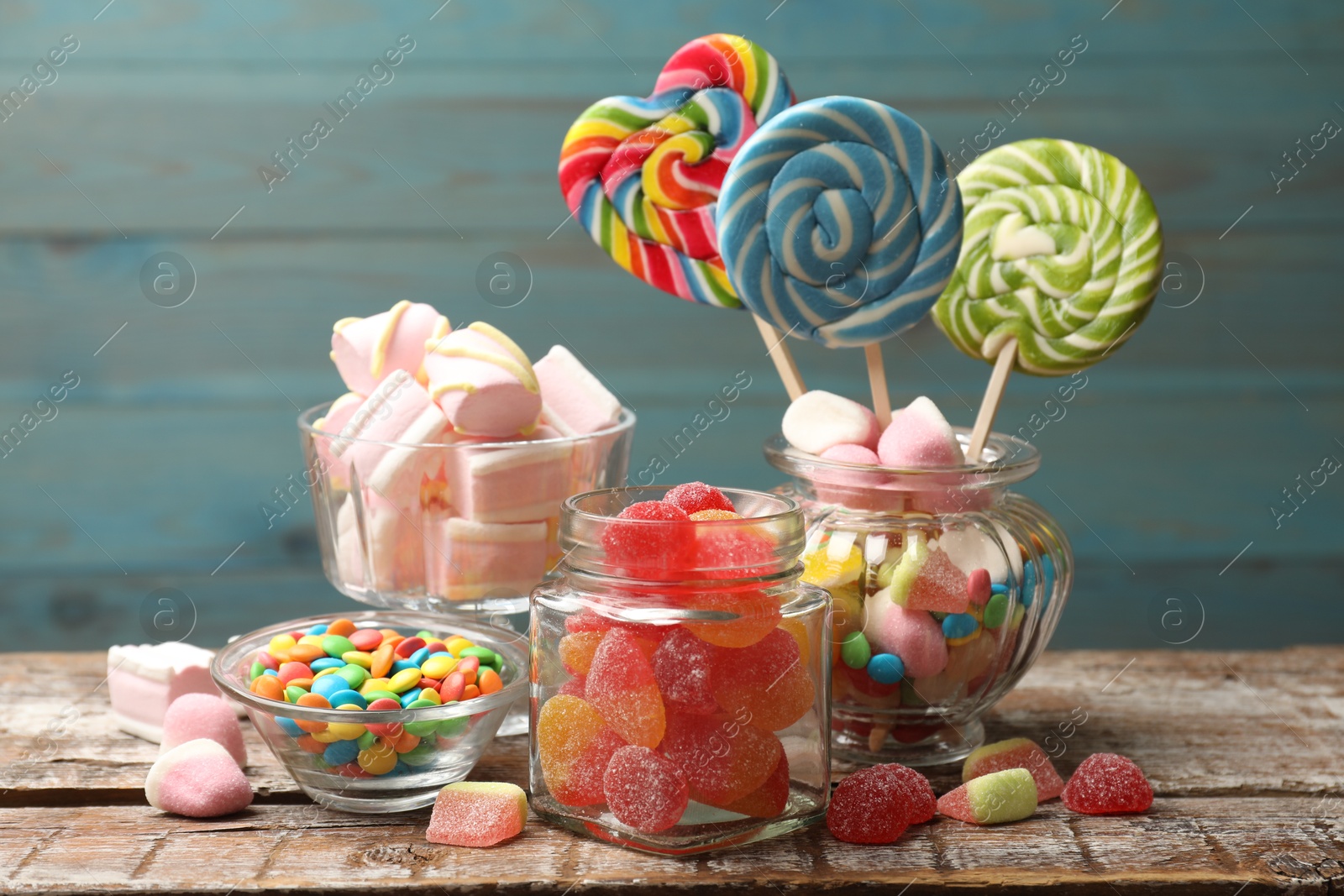 Photo of Different tasty candies on wooden table against blue background