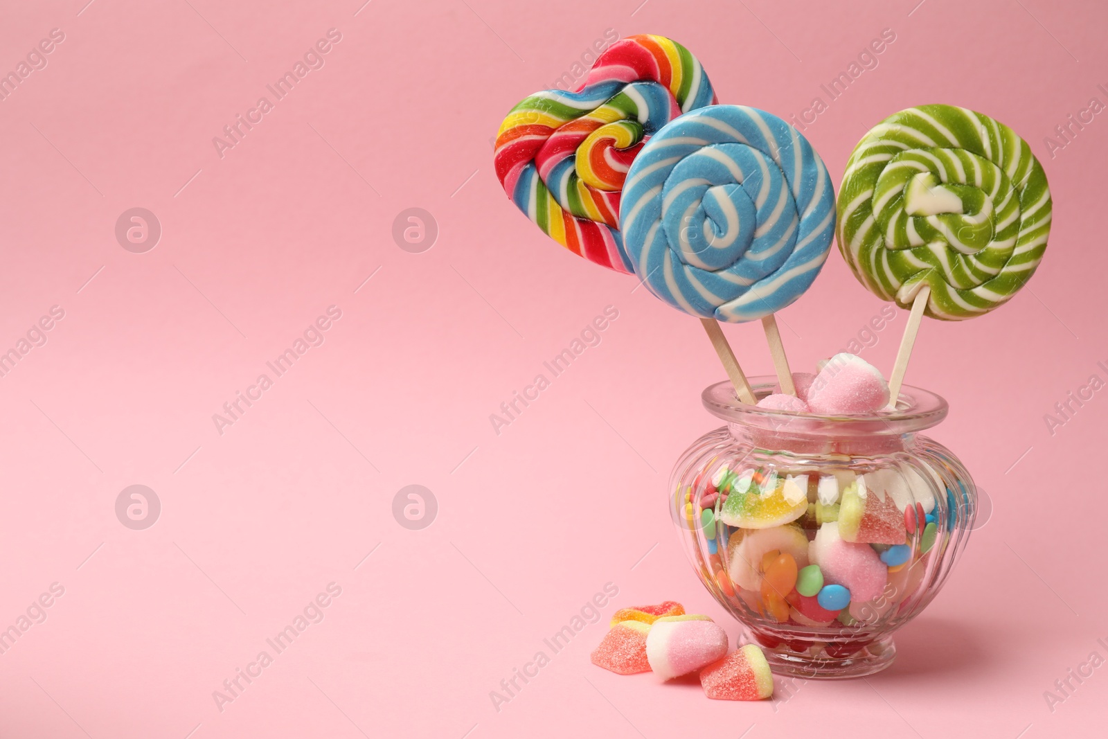 Photo of Different tasty candies in glass jar on pink background. Space for text