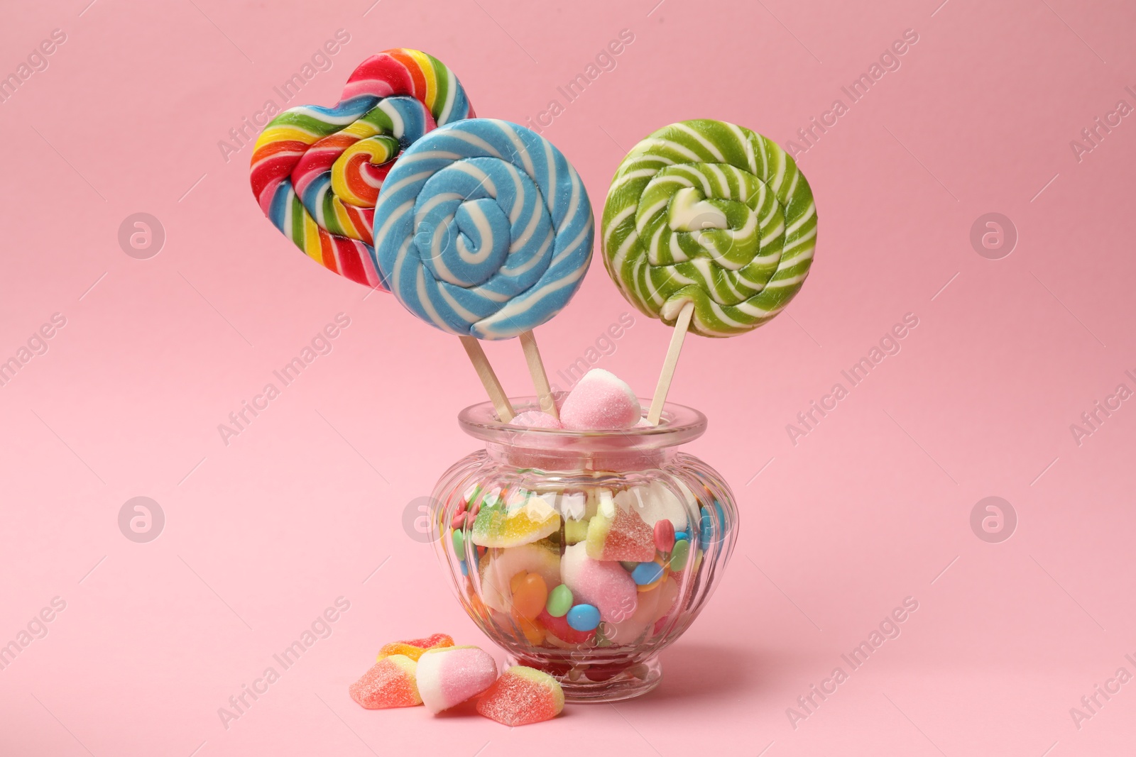 Photo of Different tasty candies in glass jar on pink background