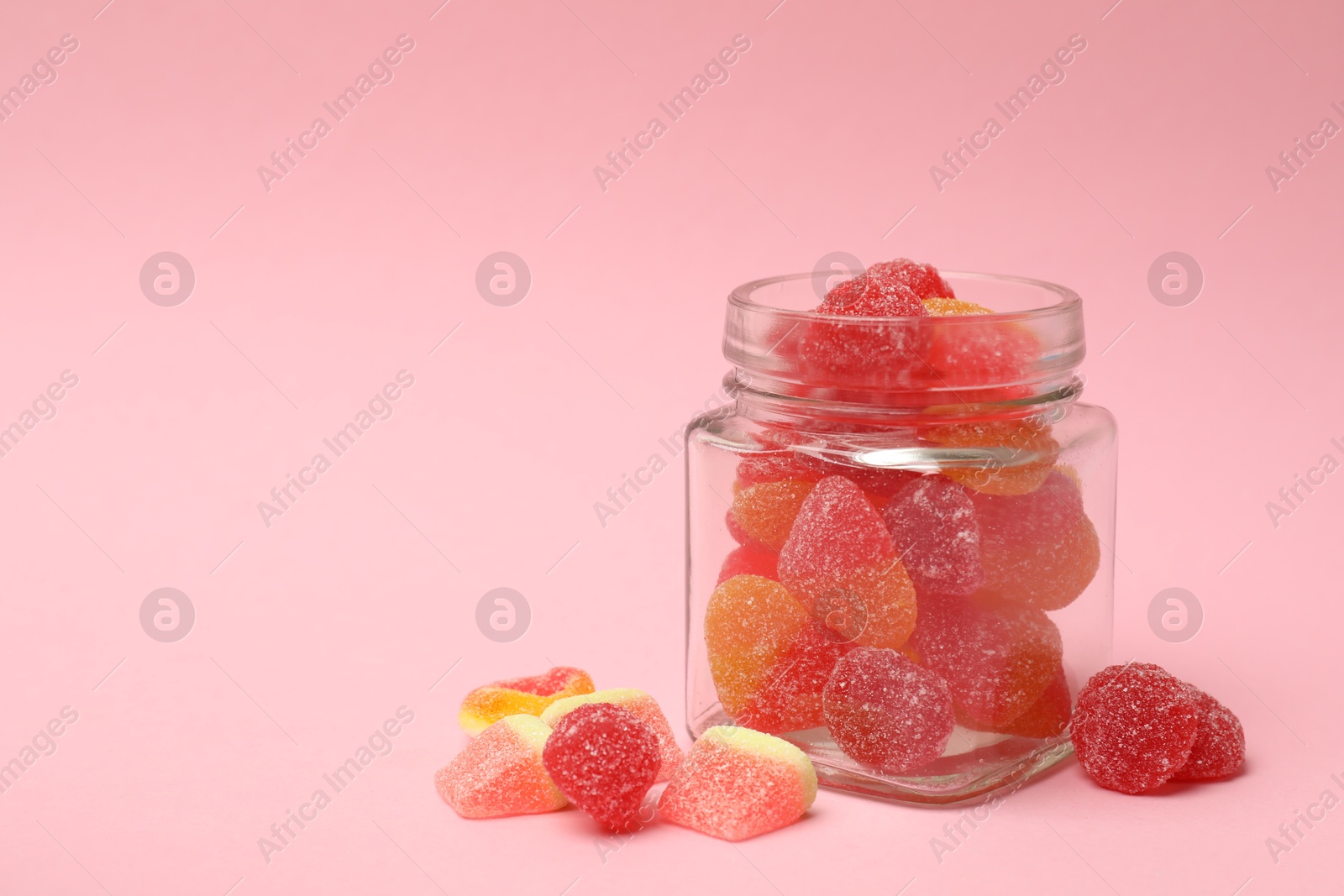 Photo of Tasty jelly candies in glass jar on pink background, closeup. Space for text