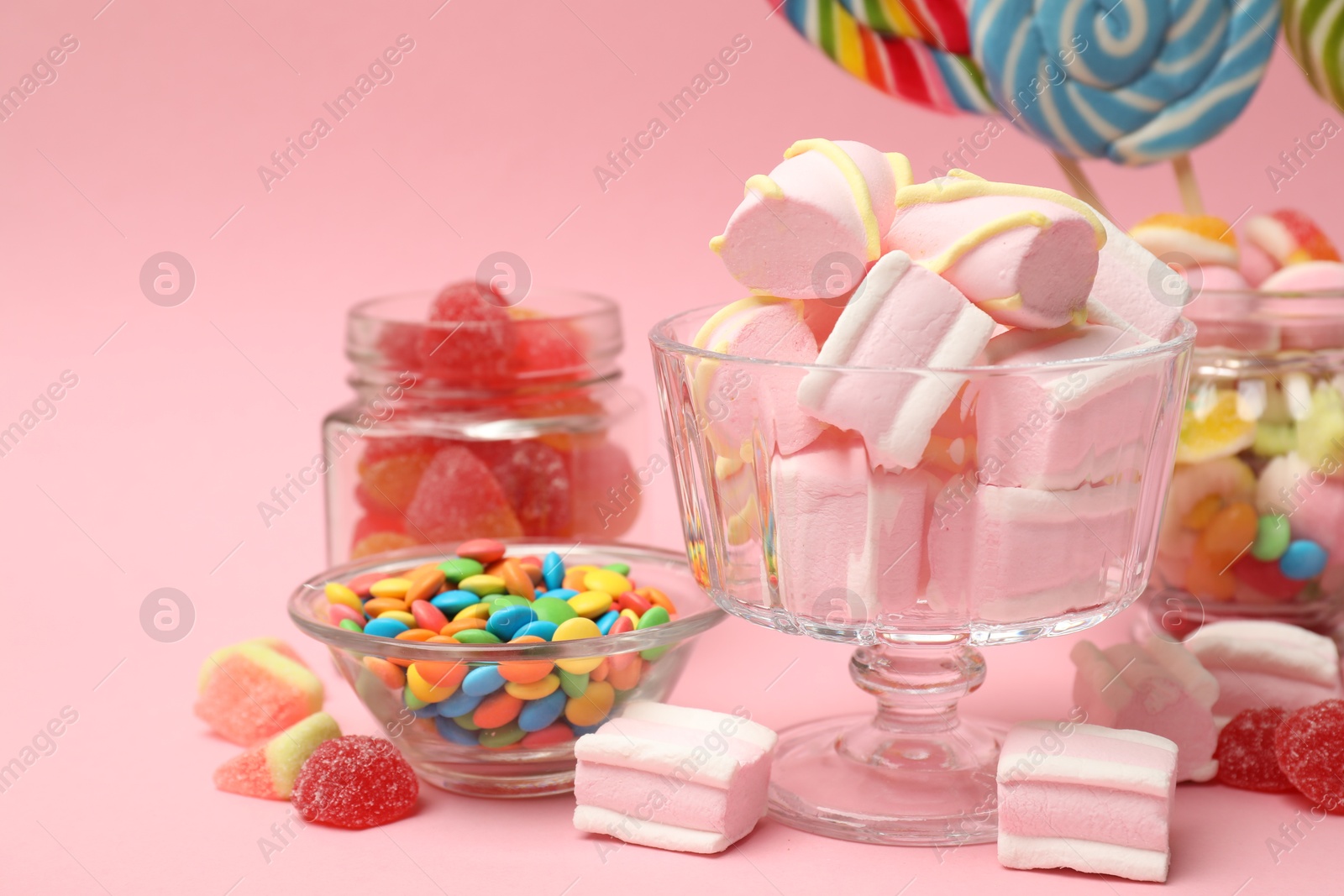 Photo of Tasty marshmallows in glass dessert bowl and candies on pink background, closeup