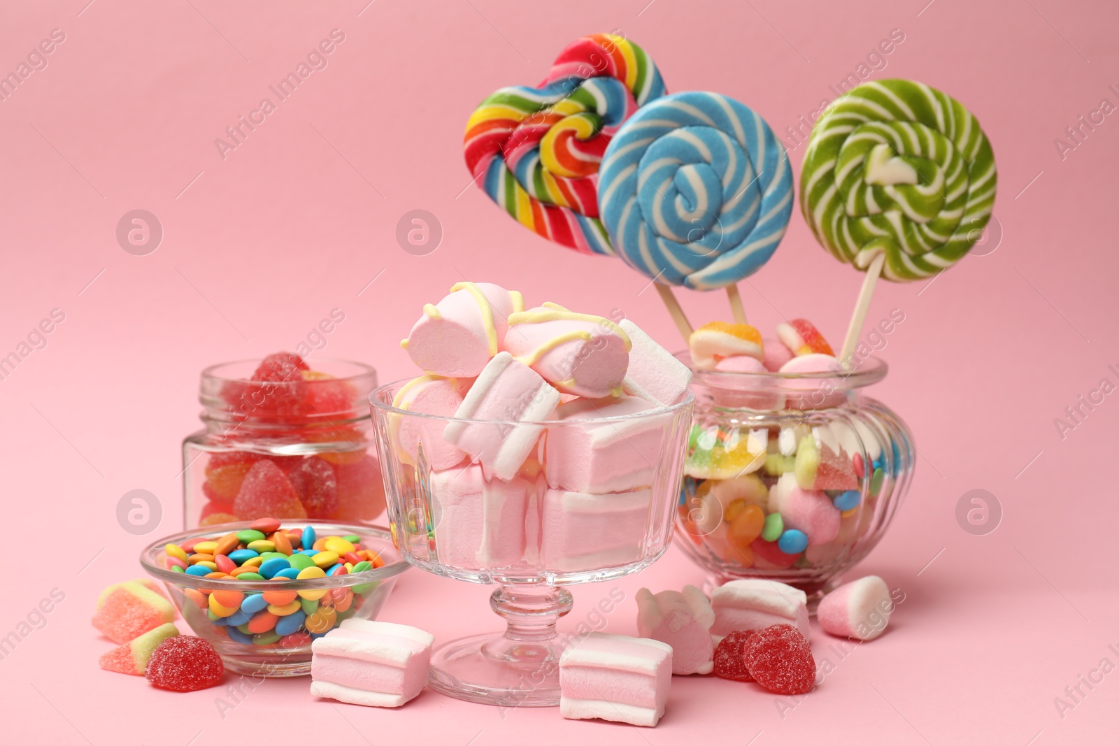 Photo of Tasty marshmallows in glass dessert bowl and candies on pink background