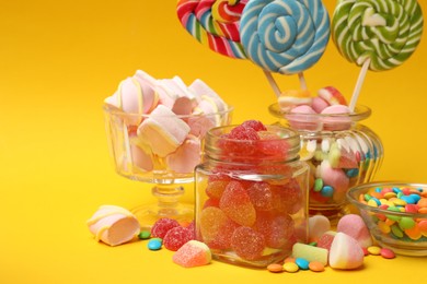 Photo of Different tasty candies on yellow background, closeup