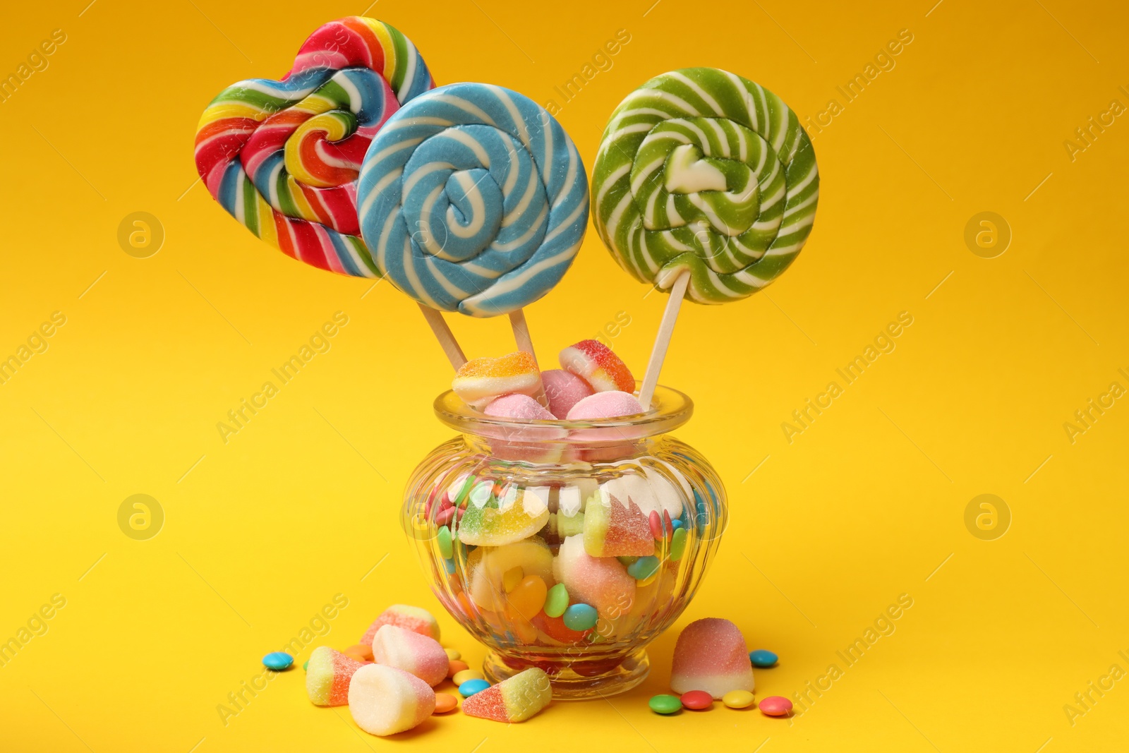 Photo of Different tasty candies in glass jar on yellow background