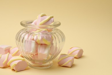 Photo of Tasty marshmallows in glass jar on beige background, closeup. Space for text