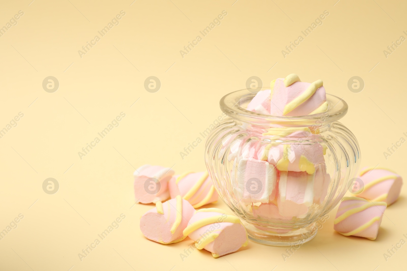 Photo of Tasty marshmallows in glass jar on beige background, closeup. Space for text