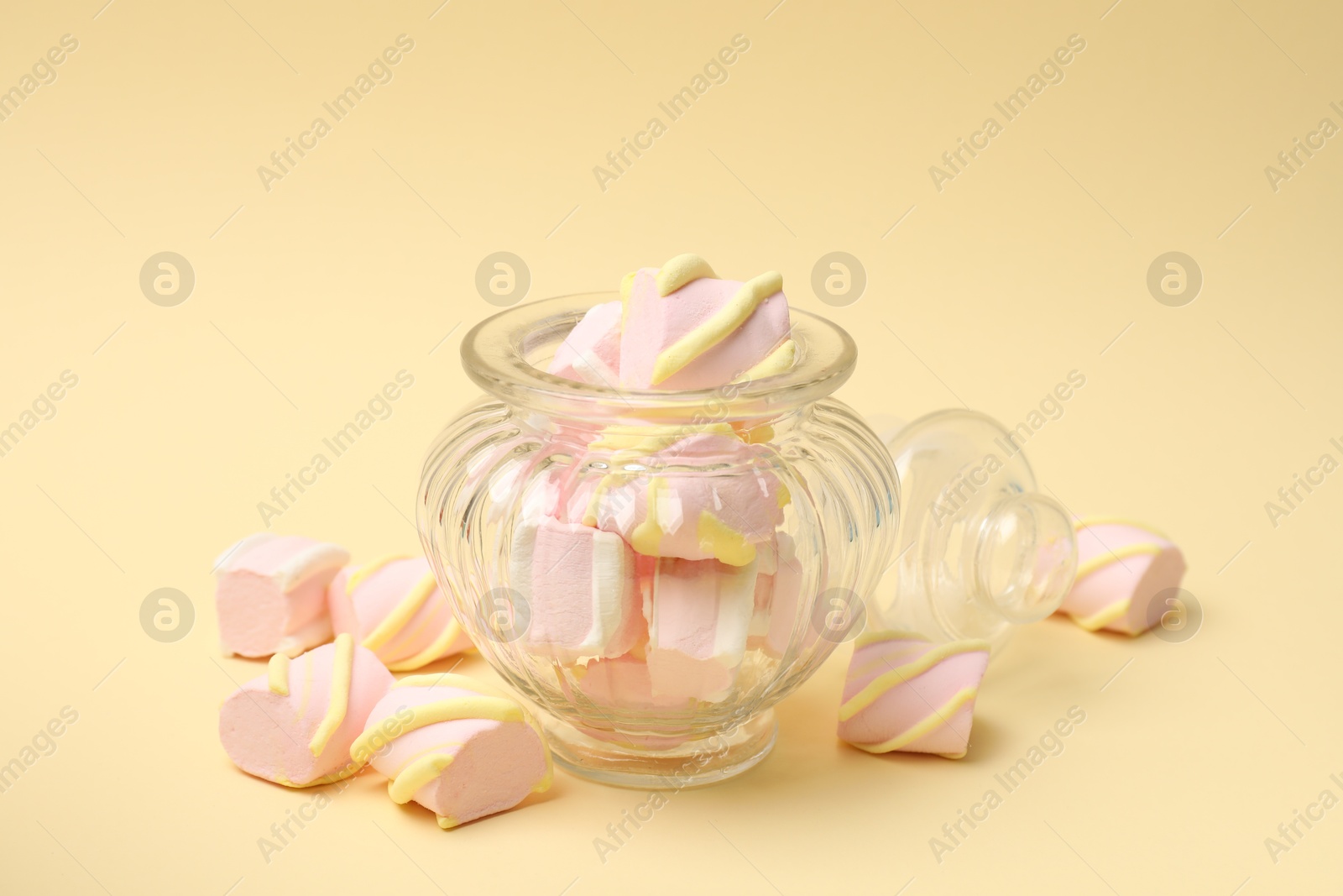 Photo of Tasty marshmallows in glass jar on beige background, closeup