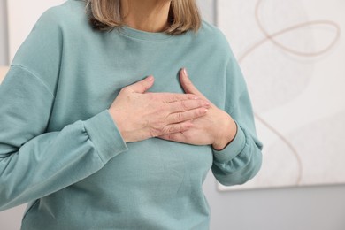 Photo of Heart attack. Senior woman suffering from pain in chest indoors, closeup