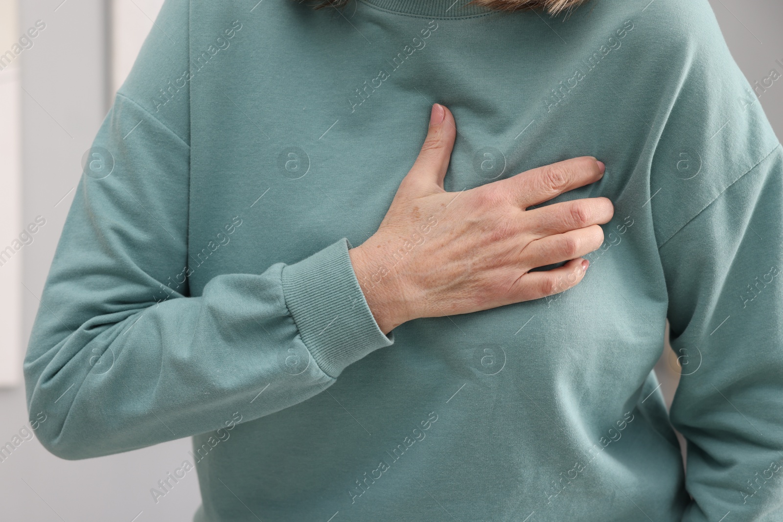 Photo of Heart attack. Senior woman suffering from pain in chest indoors, closeup