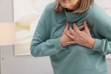 Photo of Heart attack. Senior woman suffering from pain in chest indoors, closeup