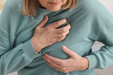 Photo of Heart attack. Senior woman suffering from pain in chest indoors, closeup