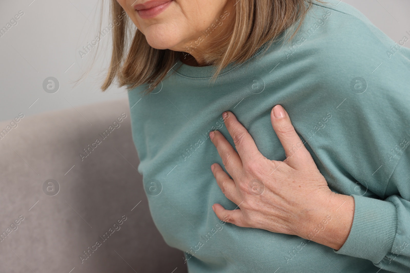 Photo of Heart attack. Senior woman suffering from pain in chest indoors, closeup