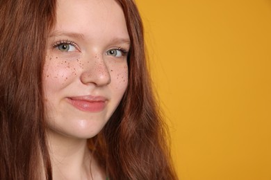 Photo of Beautiful teenage girl with freckles on orange background, closeup. Space for text